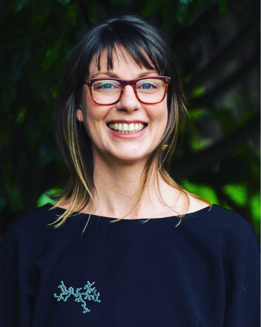 Claire Foldi, a white woman with brown hair and wearing red glasses is smiling at the camera